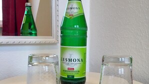 A bottle of Esmona mineral water on a white table with two empty glasses. - House Nicole vacation apartment 10 (Cuxhaven)