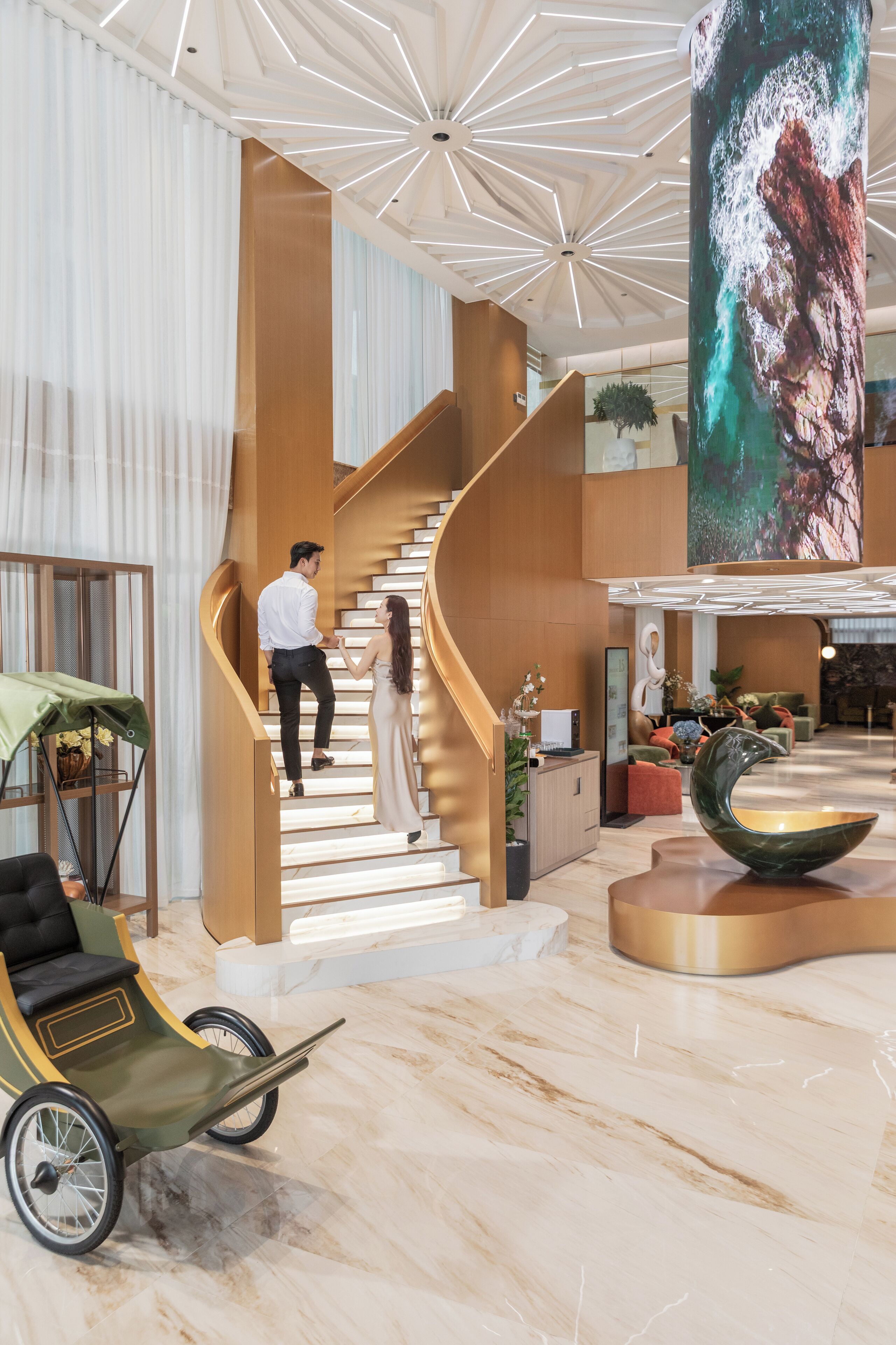 A modern hotel lobby with a spiral staircase, a large digital screen, and a carriage.