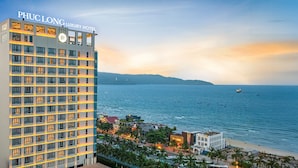 Un hotel de gran altura con varios pisos y balcones que dan a una zona costera con playa y océano.