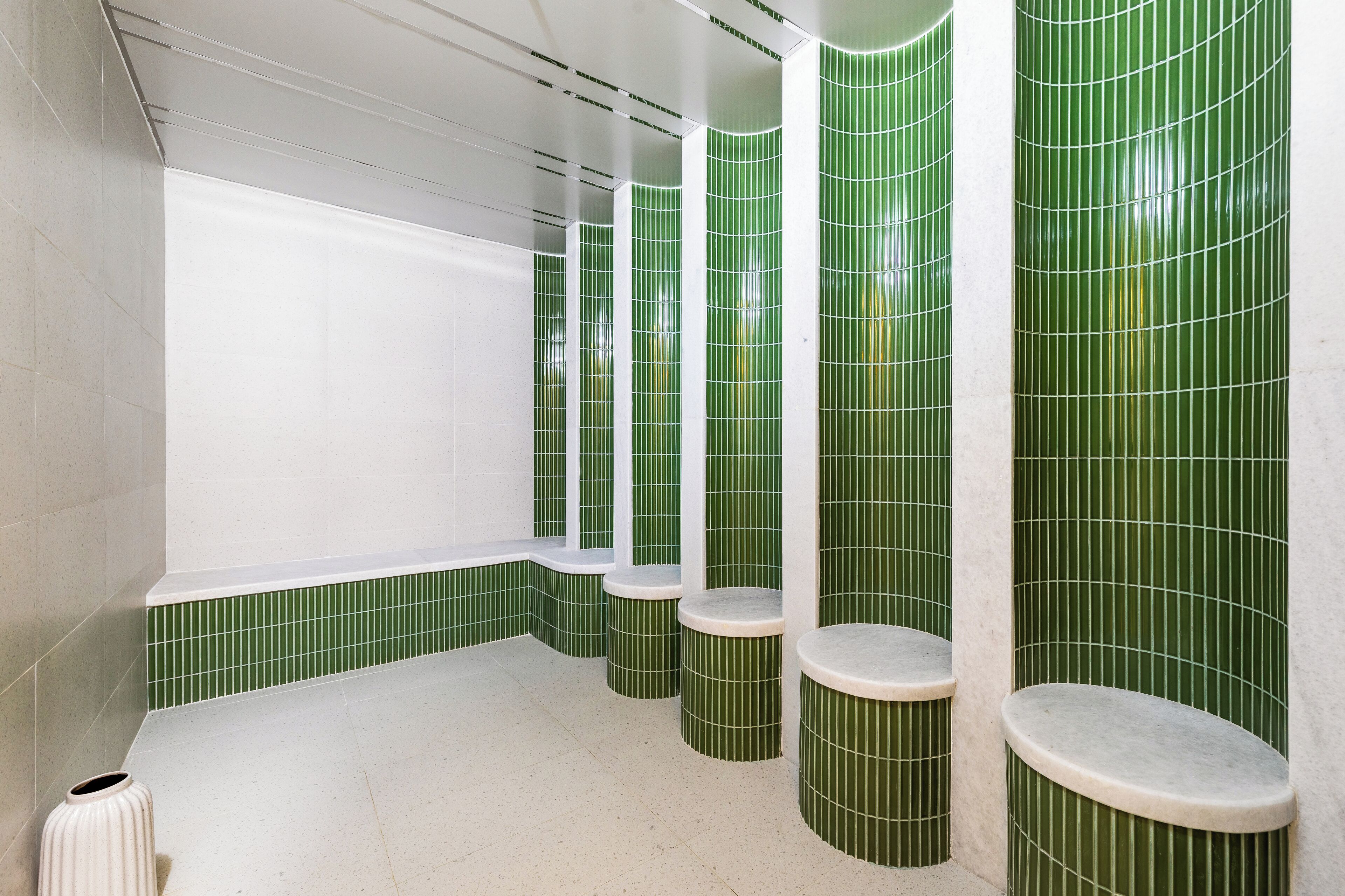 A bathroom with green tiled walls, a white bathtub, and four round stools.