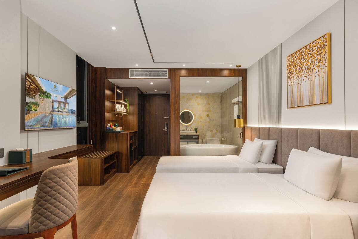 A modern hotel room with a large bed, a desk, a chair, a TV, and a bathroom with a bathtub and a mirror.