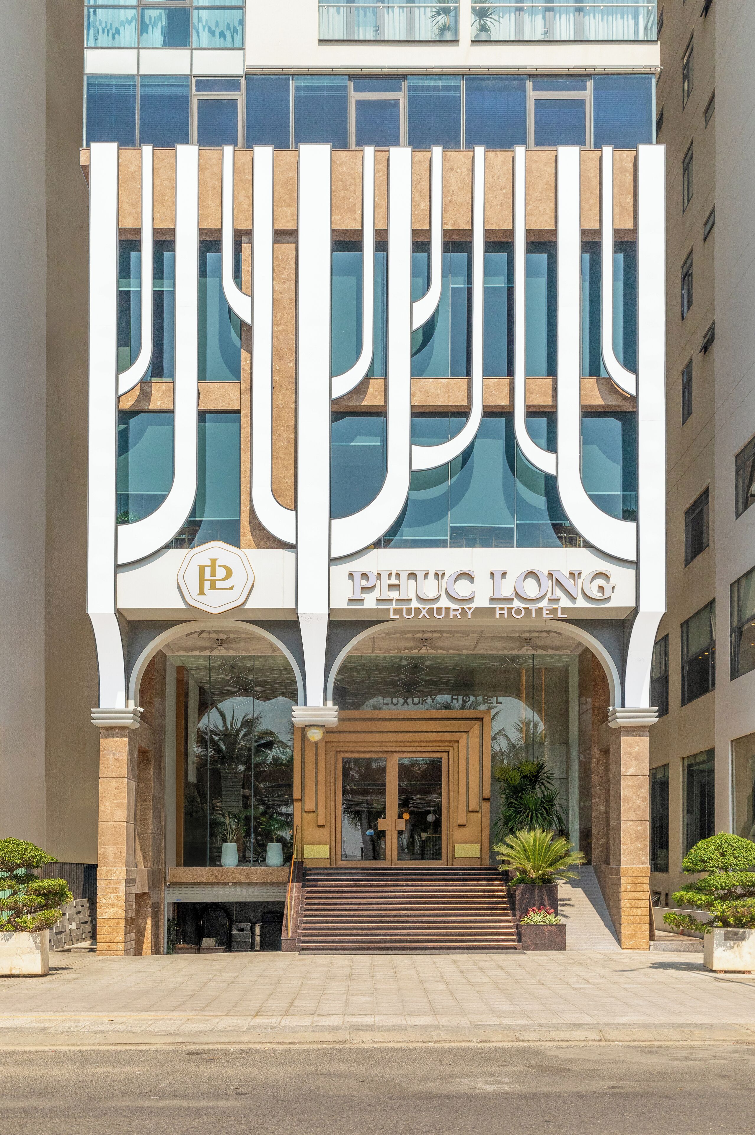 The exterior of the PHTC LONG Luxury Hotel with a modern facade, large glass windows, and a prominent entrance with steps leading up to the door.