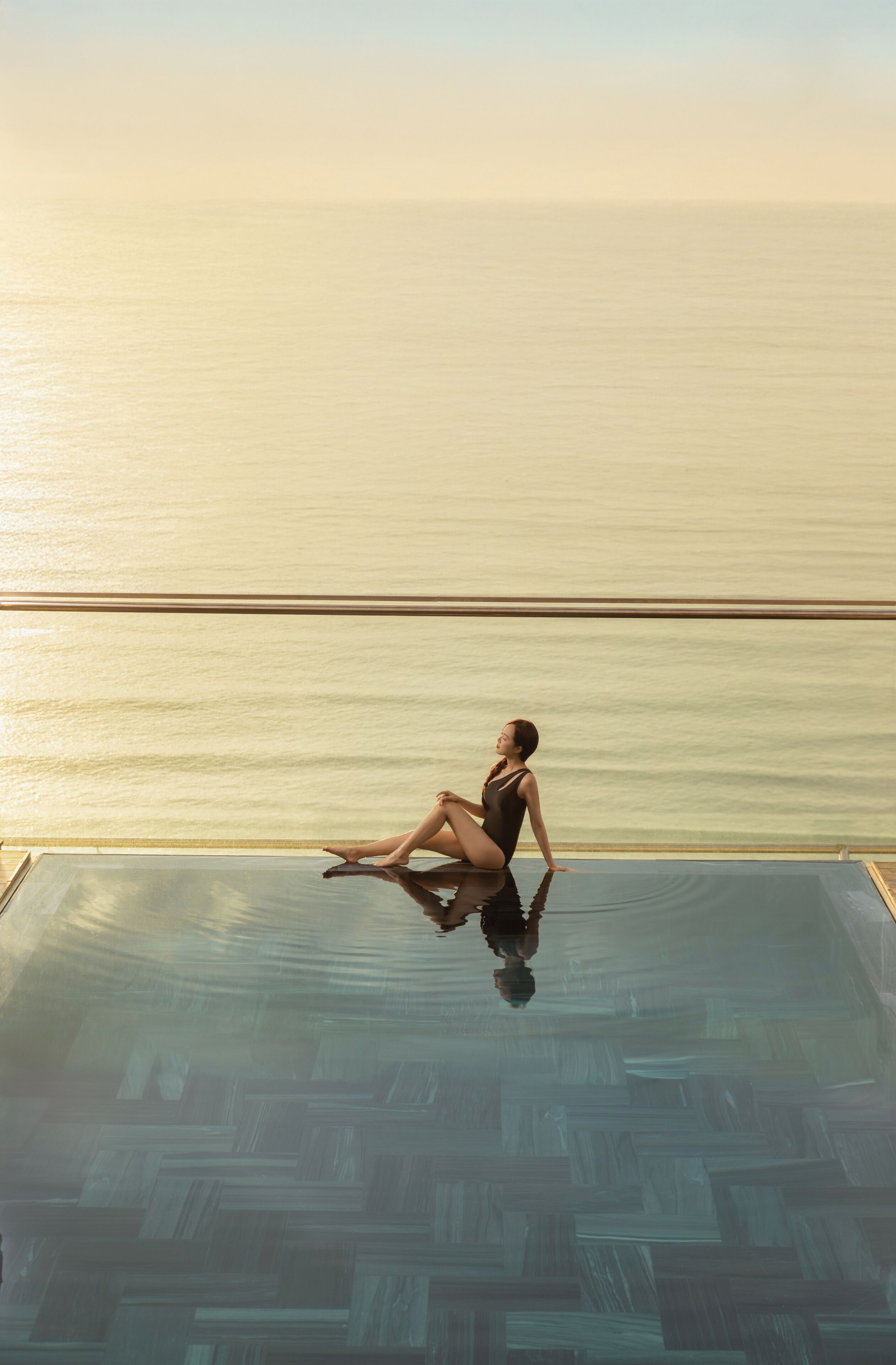 A person sitting on a glass infinity pool with a view of the sea.