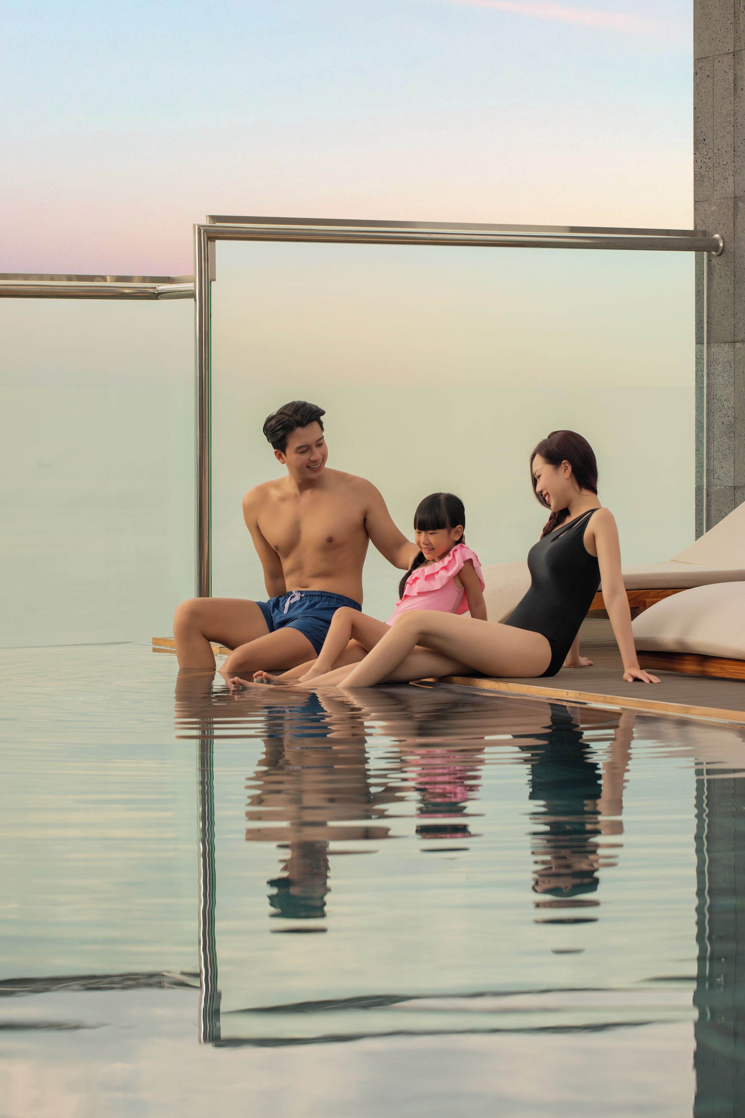A family of three by a glass-enclosed infinity pool with a clear view of the horizon.