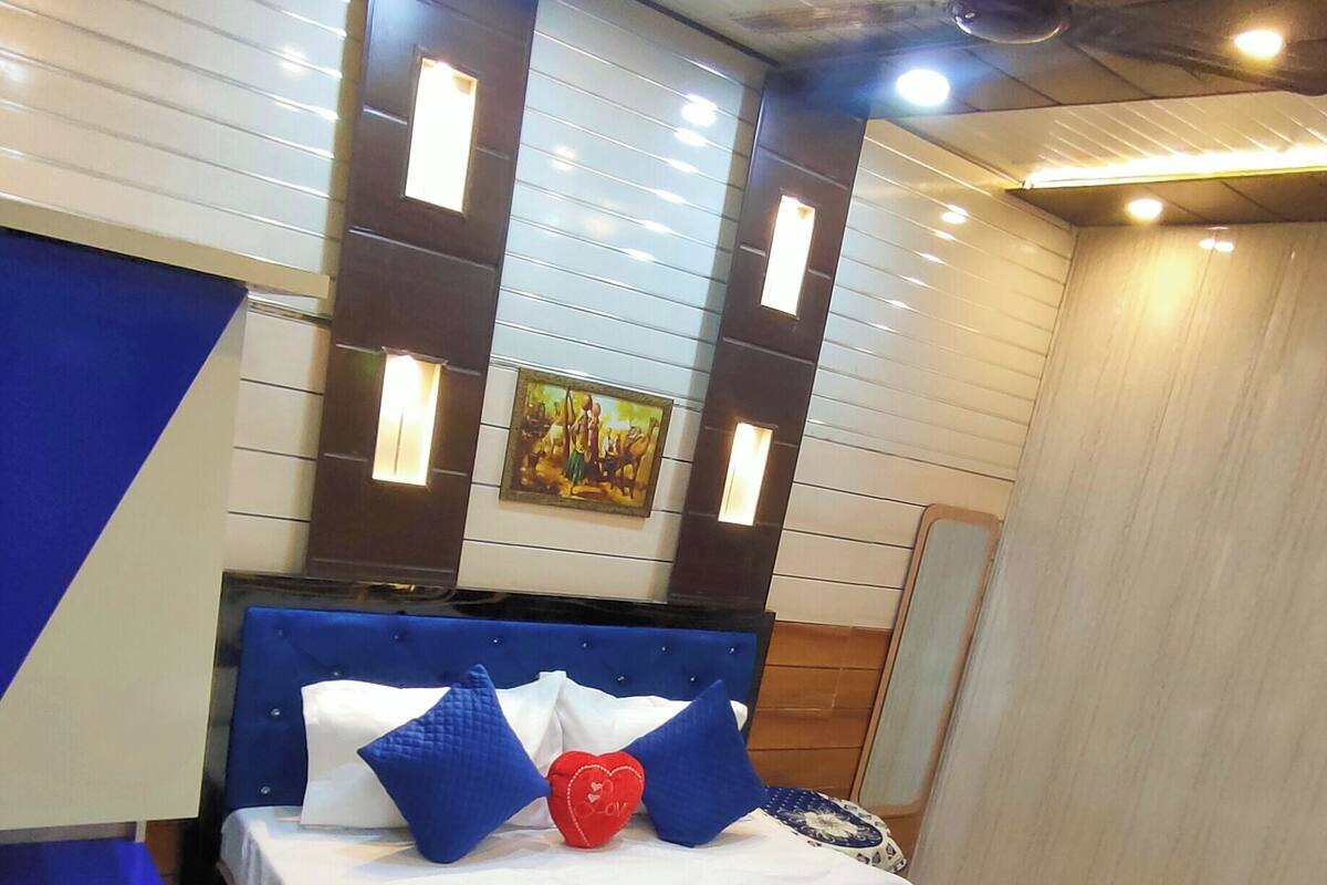 Un dormitorio moderno con una cama grande, ropa de cama azul y blanca, una almohada con forma de corazón y un cuadro en la pared.