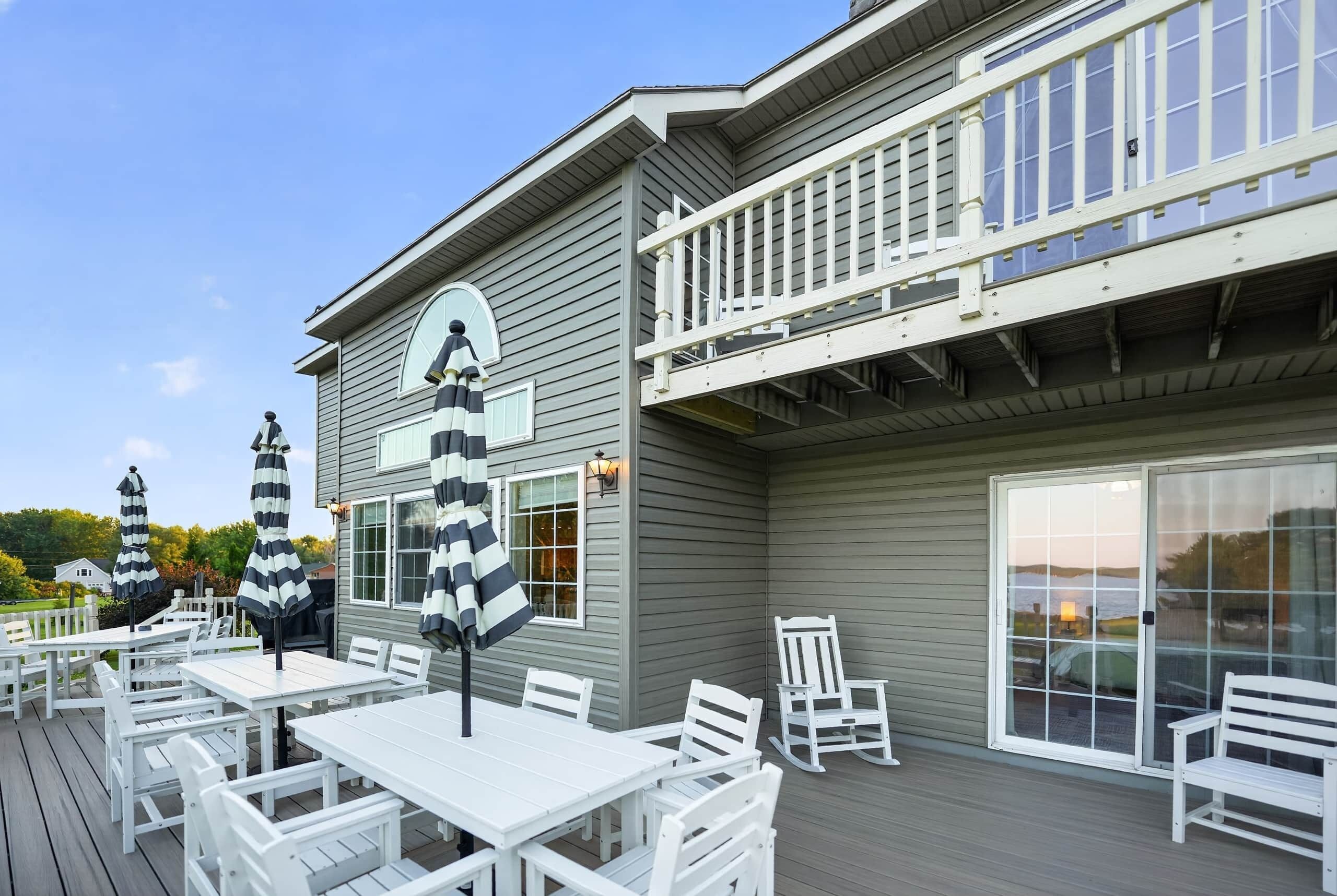 A covered outdoor seating area with white tables and chairs, a deck, and a building with a balcony.