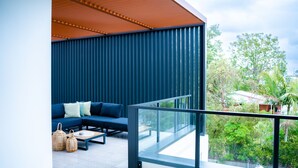 A modern balcony with a blue sofa, wicker baskets, and a glass railing overlooking a lush garden. - Happy Hour by Experience Jervis Bay (Huskisson)