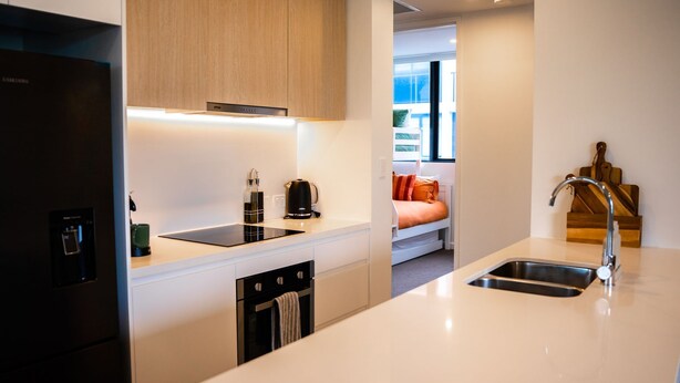 A modern kitchen with a built-in dishwasher, a coffee maker, and a kettle. There is a window with a view of the outside. - Happy Hour by Experience Jervis Bay (Huskisson)
