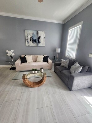 Uma sala de estar moderna com um sofá cinza claro, um sofá cinza mais escuro e uma mesa de centro de vidro com base de madeira.