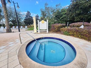 Une piscine circulaire avec un escalier en métal, entourée d’une terrasse carrelée et d’un panneau indicateur.