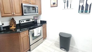 A kitchen with wooden cabinets, a microwave, a stove, and a trash bin.