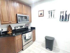 A kitchen with wooden cabinets, a microwave, a stove, and a trash bin. - 1 Min to Disney! Resort Condo w/Pool & Wifi (Kissimmee)