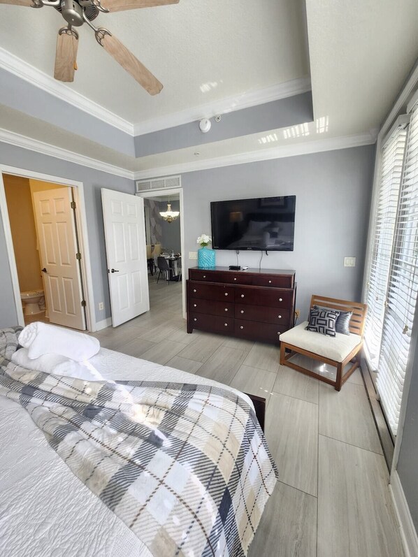 Een slaapkamer met een bed, een dressoir, een televisie en een plafondventilator.