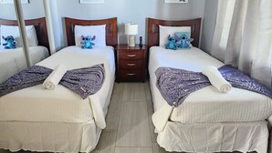 A hotel room with two beds, each with a pillow and a blanket, a bedside table with a lamp, and a mirror.