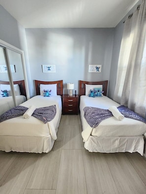 A hotel room with two beds, each with a pillow and a blanket, a bedside table with a lamp, and a mirror. - 1 Min to Disney! Resort Condo w/Pool & Wifi (Kissimmee)