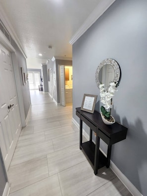 A hallway with a dark console table, a framed welcome sign, and a decorative mirror. - 1 Min to Disney! Resort Condo w/Pool & Wifi (Kissimmee)
