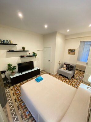 A modern bedroom with a large bed, a flat-screen TV, a small sofa, and a decorative shelf with plants. - Rooms Balmes (Barcelona)