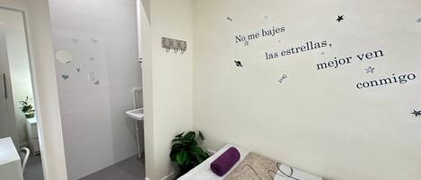 A bedroom with a bed, a wall with a motivational quote, a potted plant, and a bathroom visible through an open door.