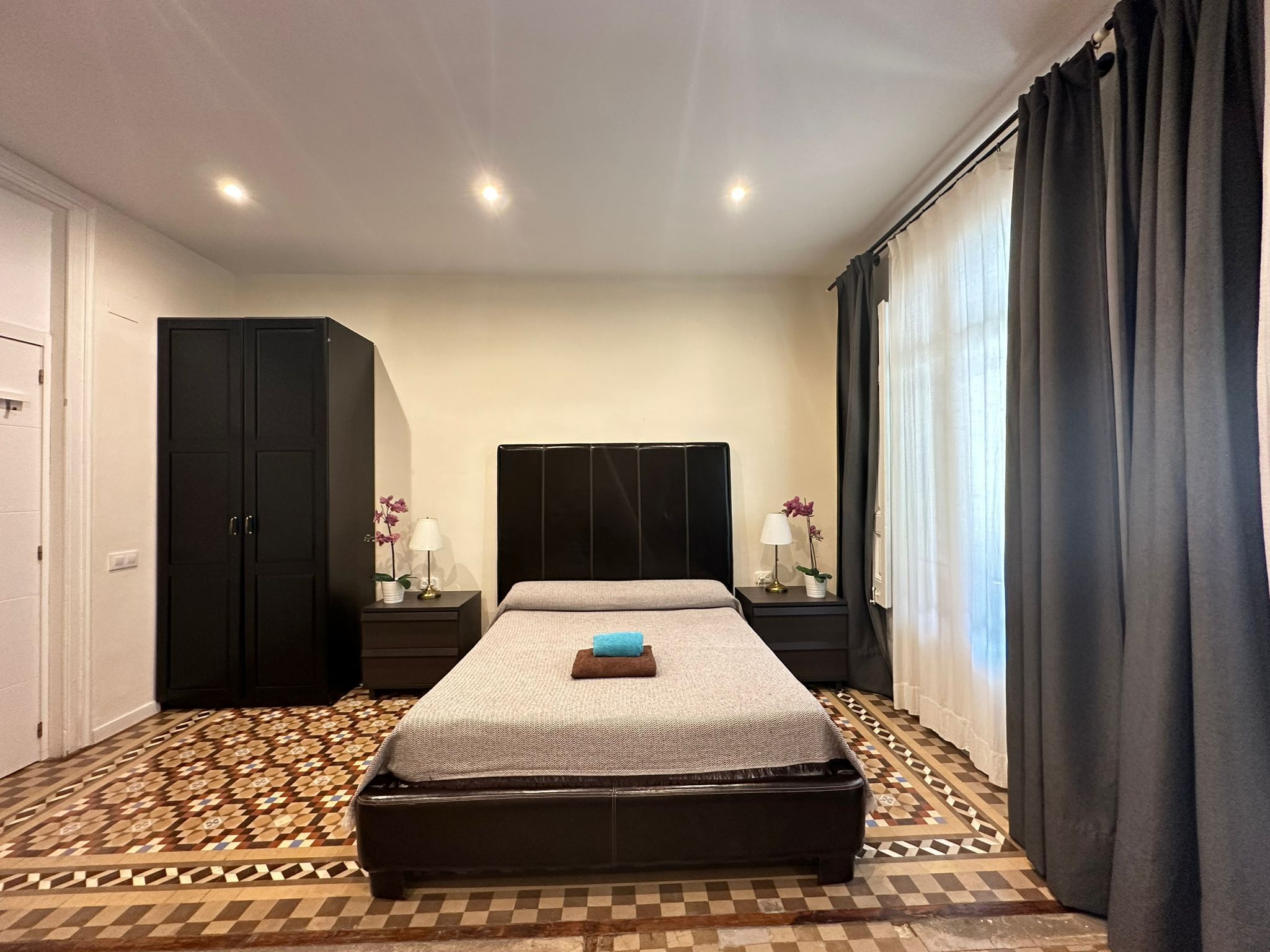 Una camera da letto con un letto grande, due comodini con lampade, un armadio e un pavimento decorato.