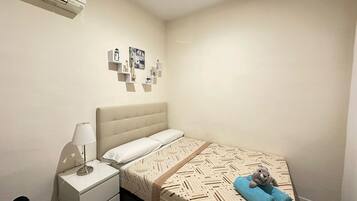 Un dormitorio pequeño y ordenado con cama, mesita de noche, lámpara y adornos en la pared.