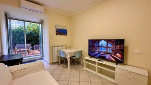 Un soggiorno con TV, divano, tavolo da pranzo e una porta a vetri scorrevoli che dà su uno spazio esterno.