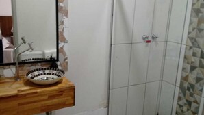 A bathroom with a wooden vanity, a sink with a bowl, a mirror, and a shower area with tiled walls. - Pousada Oca (Holambra)