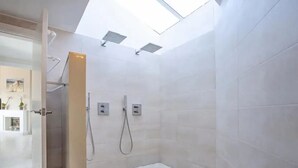 Un baño moderno con tragaluz, paredes de azulejos blancos y panel de control de ducha a la vista.