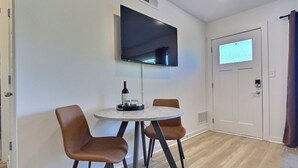 Ein Zimmer mit einem flachbildfernseher an der Wand, einem runden Tisch mit zwei Stühlen und einer Tür mit Fenster.