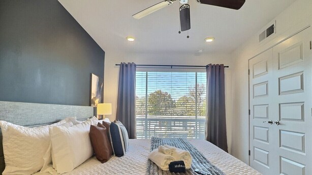 Ein Hotelzimmer mit Bett, Kissen, Decke, Deckenventilator und Blick ins Freie durch ein Fenster.