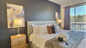 Ein Schlafzimmer mit einem großen Bett, einem Nachttisch, einer Lampe und Blick ins Freie.