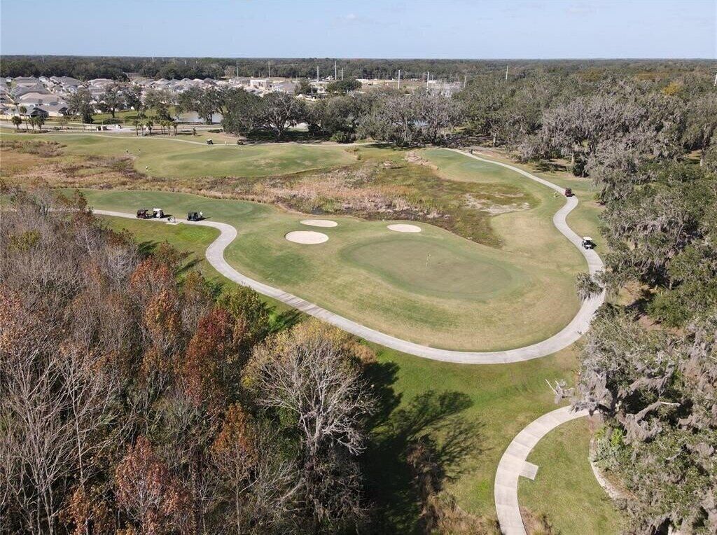 An aerial view of a golf course with multiple holes, surrounded by trees and residential areas.