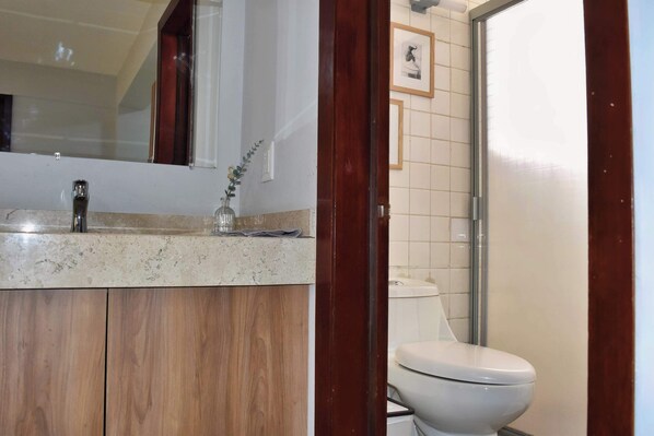 Ein Badezimmer mit einem Holzkonsolenunterschrank, einer Glasvase und einer weißen Toilette.