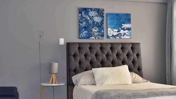 A bedroom with a tufted headboard, a bed with white and gray bedding, a small round table with a lamp, and two floral paintings on the wall. - Beautiful Department in the Historic Center. 201 (San Luis Potosí)