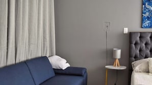 A room with a dark blue sofa, a bed with a tufted headboard, a small round table with a lamp, and a painting on the wall. - Beautiful Department in the Historic Center. 201 (San Luis Potosí)