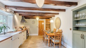 Une cuisine avec des poutres en bois, une table à manger avec des chaises, une horloge et une étagère avec des verres.