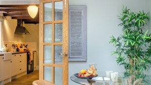 Une cuisine moderne avec des meubles blancs, une porte en bois et un coin repas comprenant une table en verre et une plante.