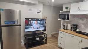 A modern kitchen with a stainless steel refrigerator, a flat-screen TV mounted on a black stand, a microwave, and a coffee maker on the counter. - Welcoming Private 2 Bedroom Suite (Winnipeg)