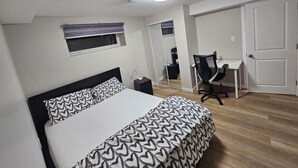 A bedroom with a bed, a desk, a chair, a window with blinds, a mirror, and a door. - Welcoming Private 2 Bedroom Suite (Winnipeg)