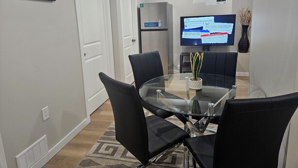 A modern conference room with a glass table, black chairs, a large flat-screen TV, and a decorative plant. - Welcoming Private 2 Bedroom Suite (Winnipeg)