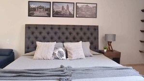 Un dormitorio con cabecera capitonada, cama con ropa de cama gris y tres cuadros en la pared.