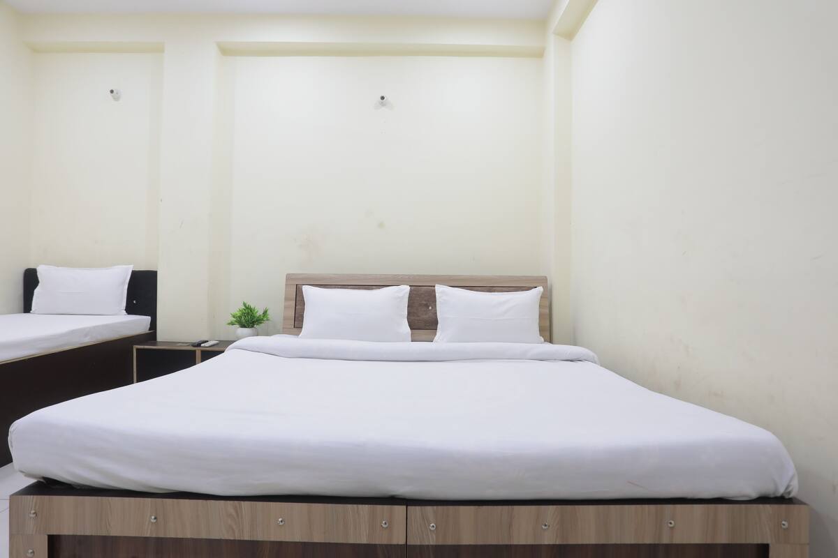 A single bed with a wooden headboard and white bedding, a small bedside table with a plant, and a white wall.