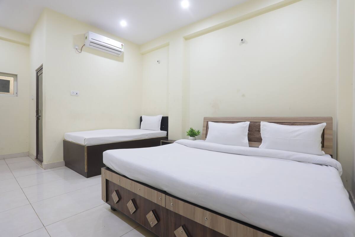 A hotel room with two single beds, a wooden headboard, a small potted plant, and an air conditioning unit on the wall.