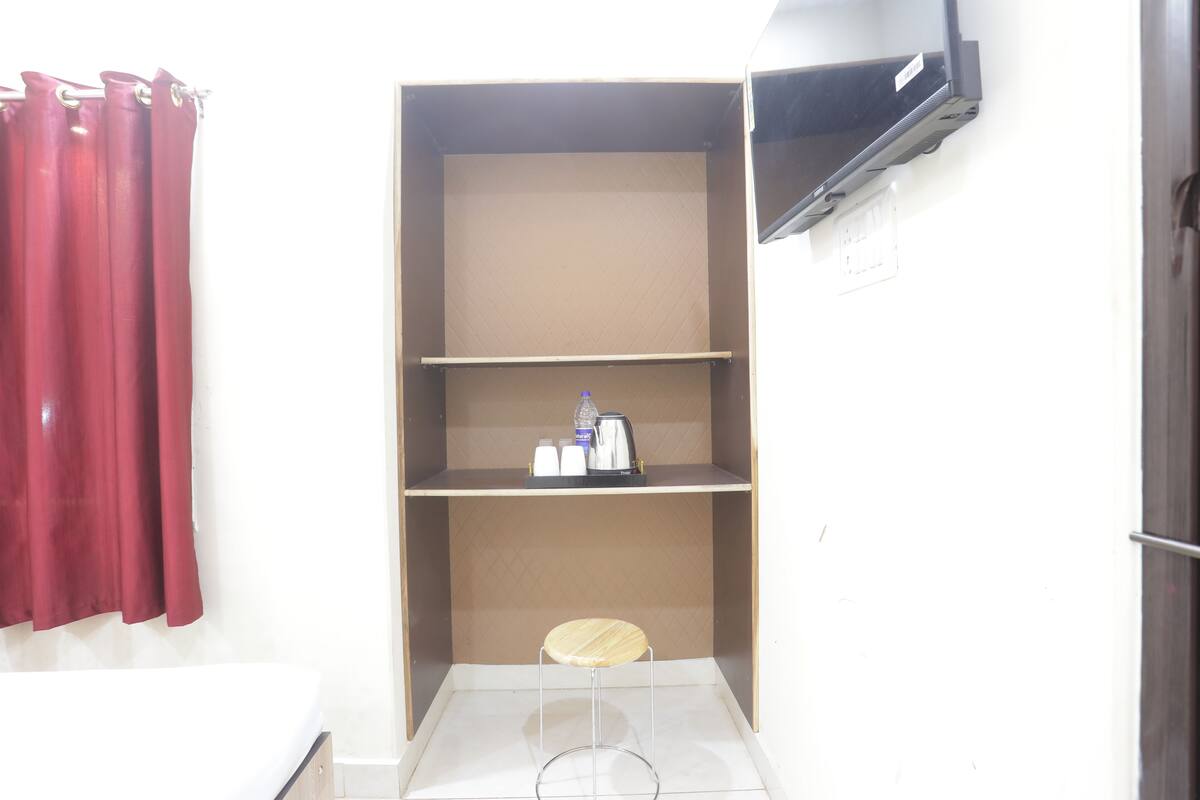 A small room with a single stool, a shelf with a kettle and cups, and a red curtain.