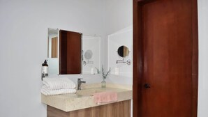 A bathroom with a wooden vanity, a sink, a mirror, and a door. - Céntrico y Confortable Departamento 101 (San Luis Potosí)