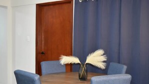 A round wooden table with four blue chairs, a vase with white feathers, and a closed wooden door. - Céntrico y Confortable Departamento 101 (San Luis Potosí)