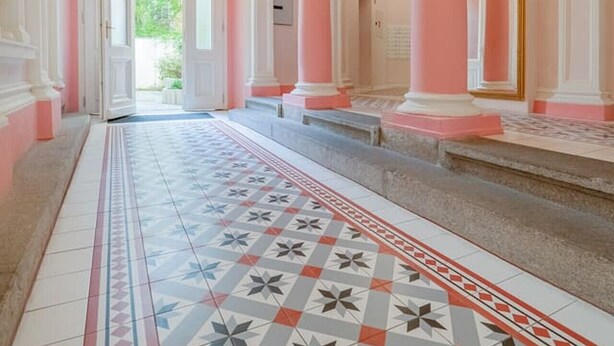 A grand hallway with pink columns, a patterned floor, and a chandelier.