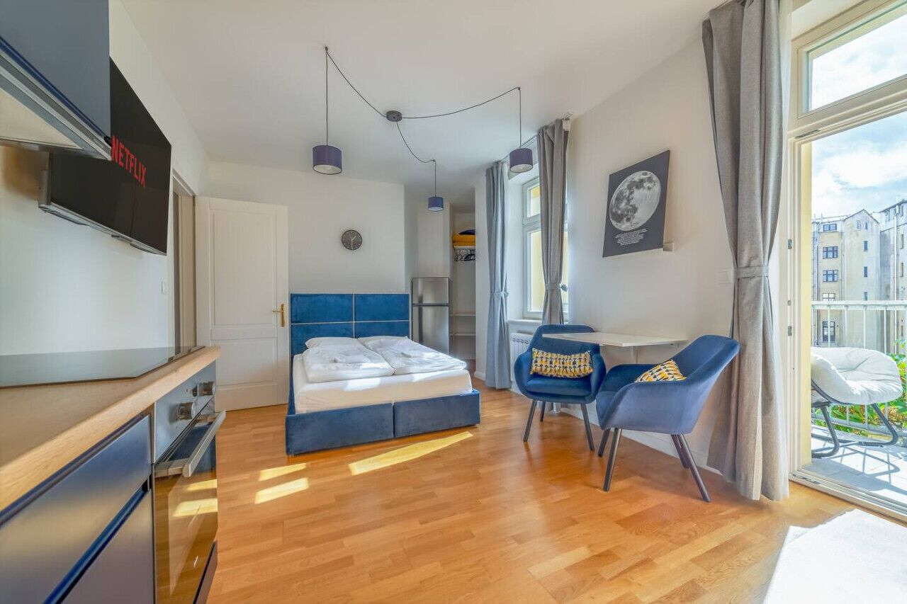 Et moderne hotelværelse med seng, skrivebord, stol, fjernsyn og et vindue med udsigt til bygninger.
