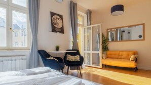 A modern bedroom with a large bed, a desk, a chair, a sofa, and a large window.