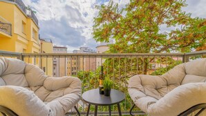 A balcony with two cushioned chairs and a small table, a bottle of wine, and a potted plant.