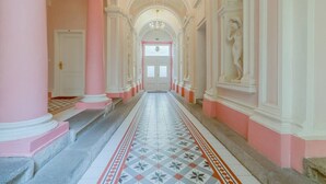 A grand hallway with pink and white columns, a patterned floor, and a chandelier.